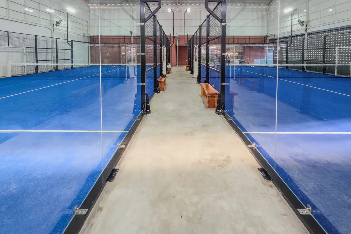 Two rows of indoor padel courts with blue turf and glass walls